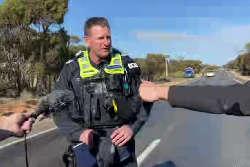 A policeman speaking to reporters on a road.