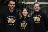 Three teens stand smiling, wearing black hooded jumpers with a bee on the front and Australia