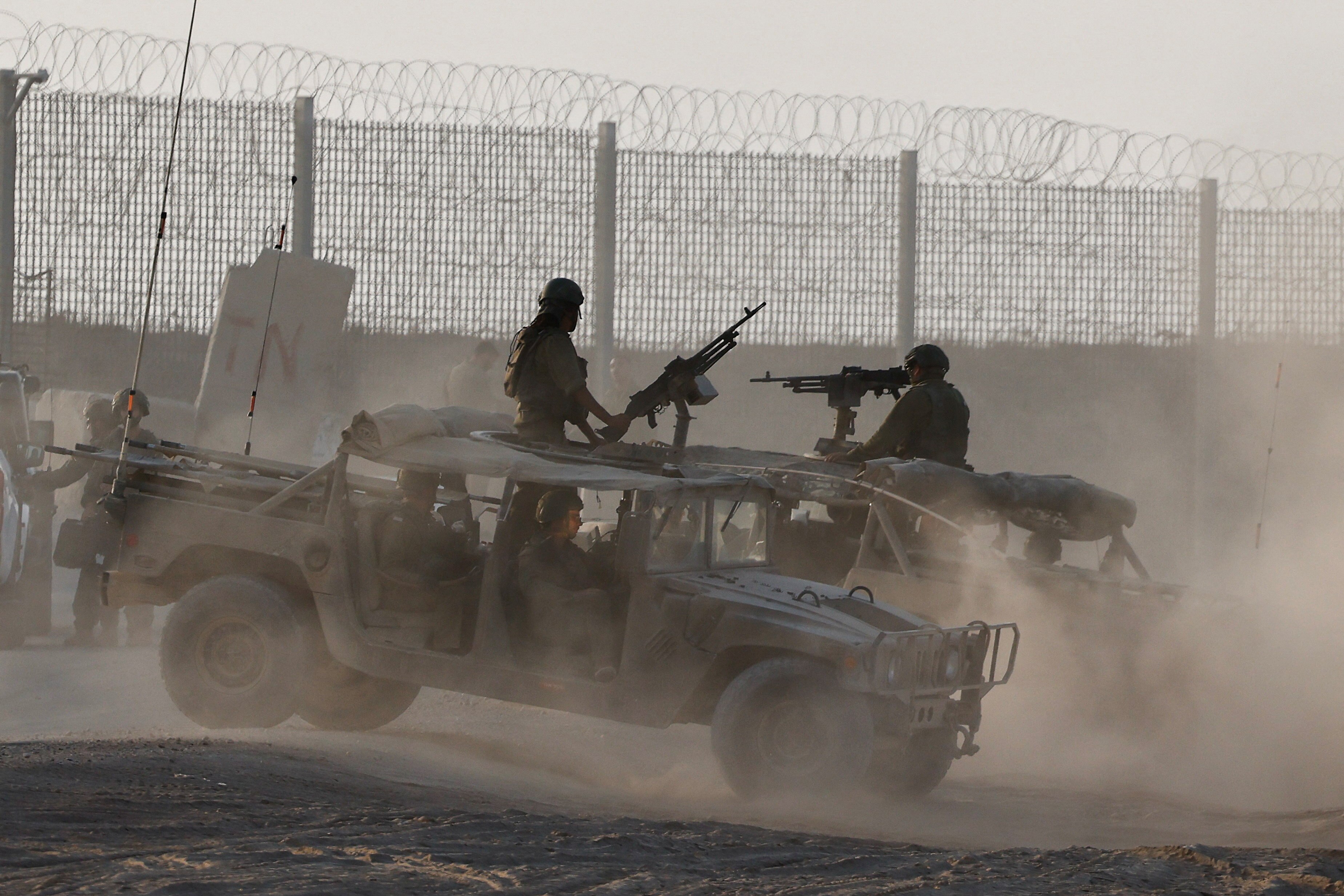 military vehicles operate in dirt track area, men holding machine guns sit atop them