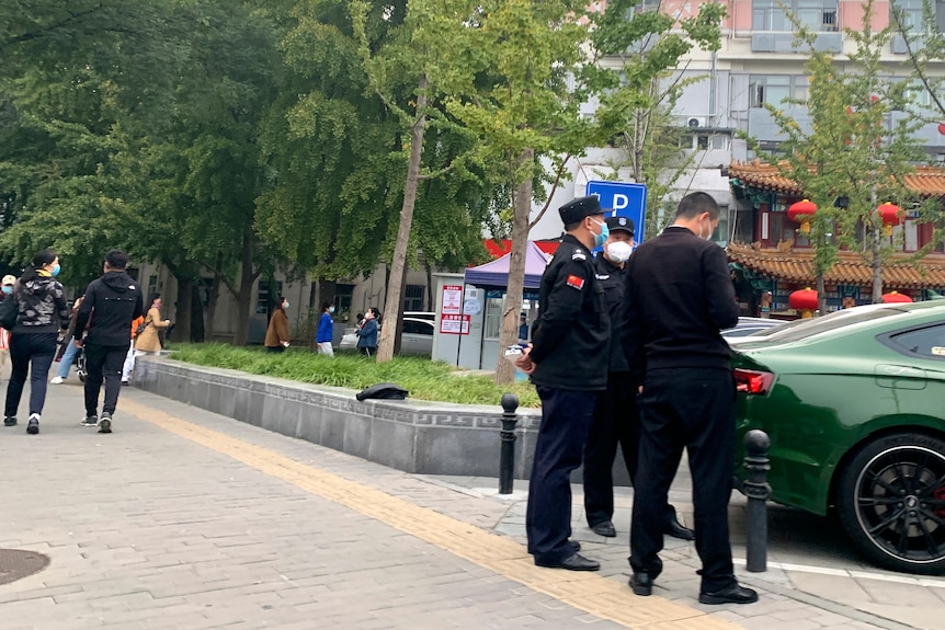 Trei ofițeri de poliție stau lângă un pod în spatele unui sedan verde.