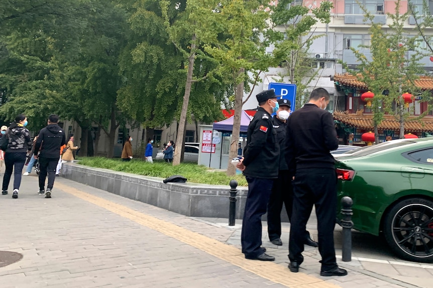 Three police officers stand near a bridge at the rear of a green sedan.