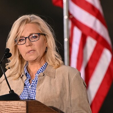 Liz Cheney has long blonde hair and she delivers her speech at a lectern in front of an American flag