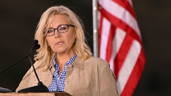 Liz Cheney has long blonde hair and she delivers her speech at a lectern in front of an American flag