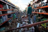 A man stands inside of a destroyed supermarket.