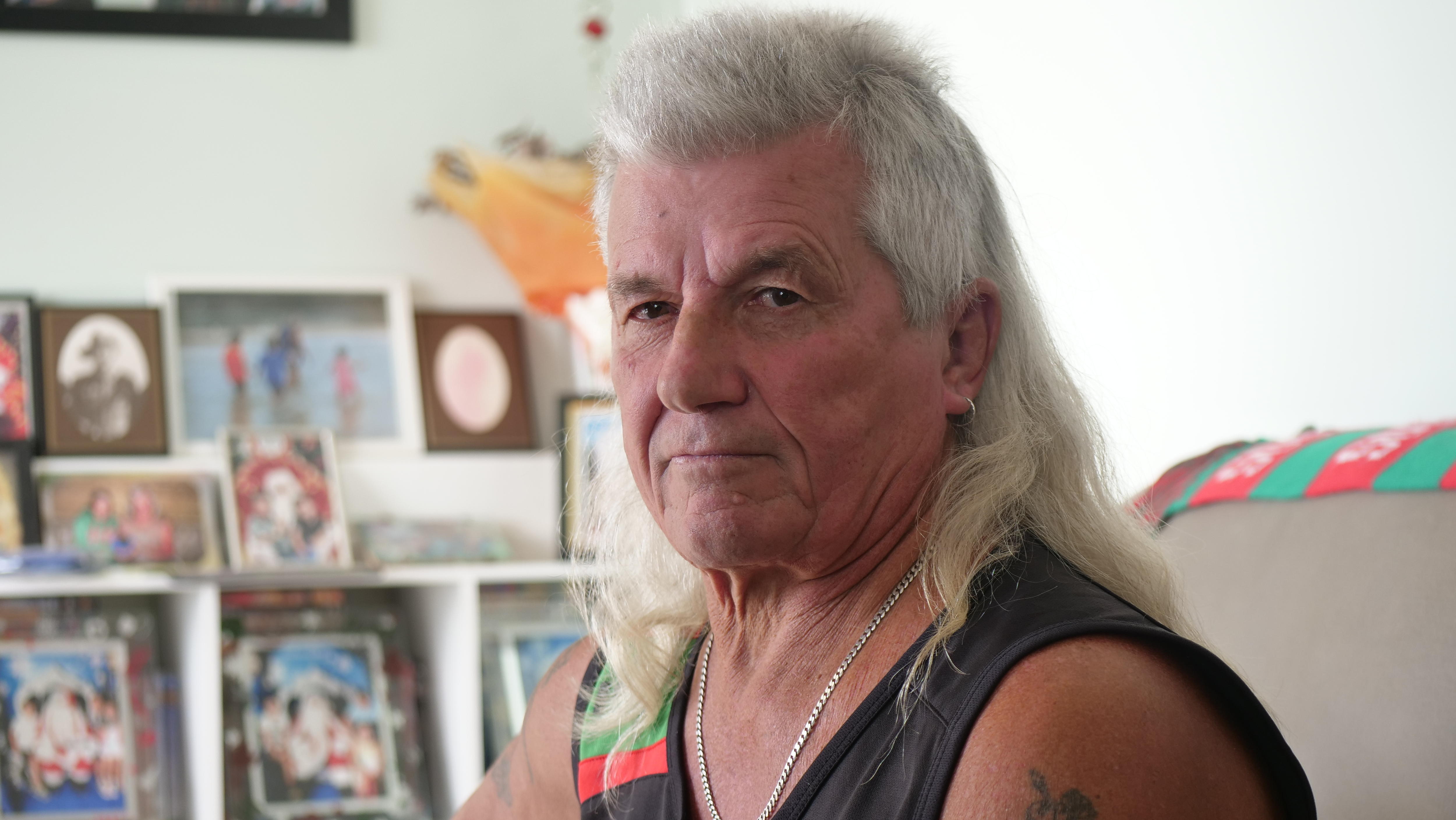 man with mullet looks at camera with photos in background