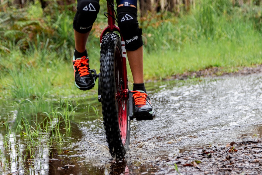 Feet on the pedals of a unicycle, travelling along a wet bush track.