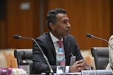 Lambo Kanagaratnam a man in a suit sitting in front of a microphone. 