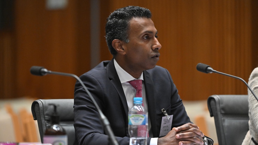 Lambo Kanagaratnam a man in a suit sitting in front of a microphone. 