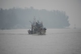 A fishing boat sails on the Narathiwat river through haze in southern Thailand