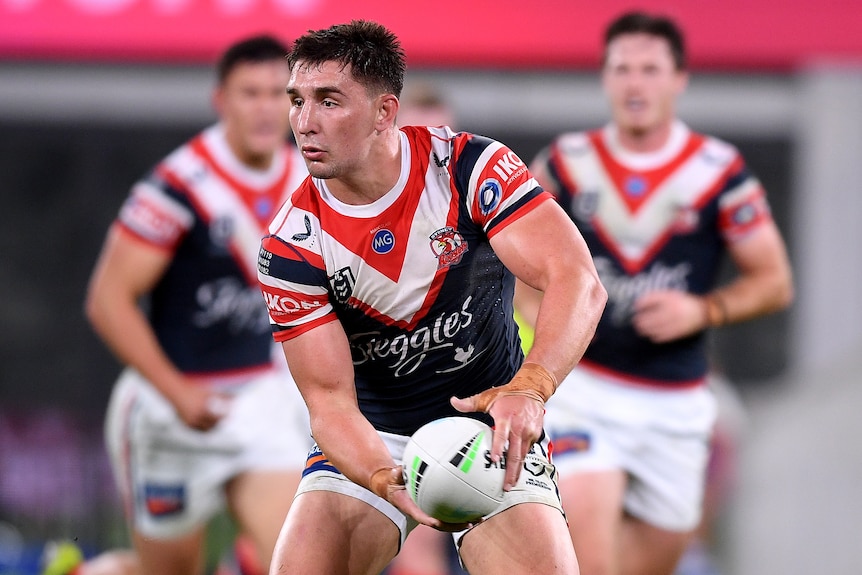 A Sydney Roosters NRL player prepares to pass the ball with both hands to his left.