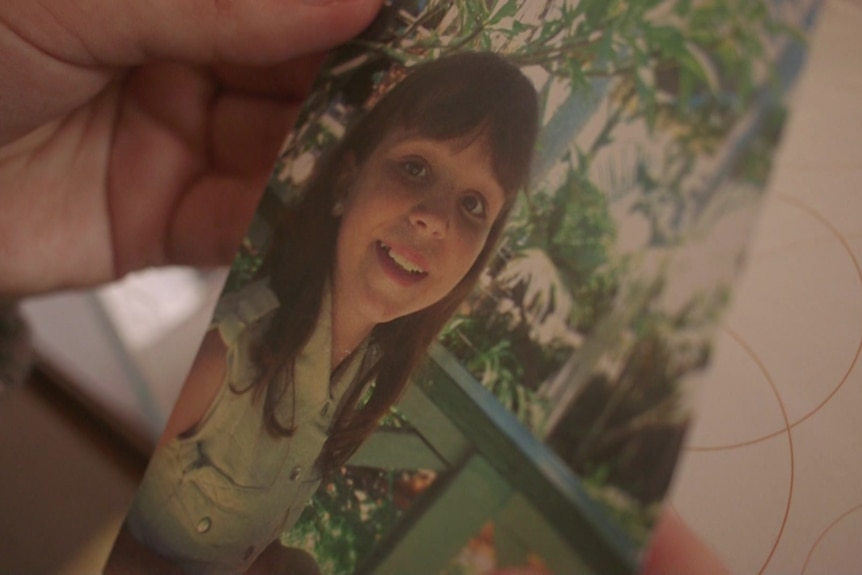 A hand holds an older film photo of a young girl. 