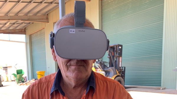 A man wearing an orange work shirt is wearing a virtual reality headset while holding a handpiece sitting down