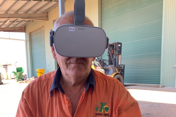 A man wearing an orange work shirt is wearing a virtual reality headset while holding a handpiece sitting down