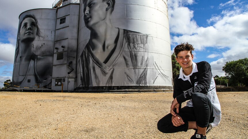 Jordan Weidemann crouching in front the giant steel silo bins.