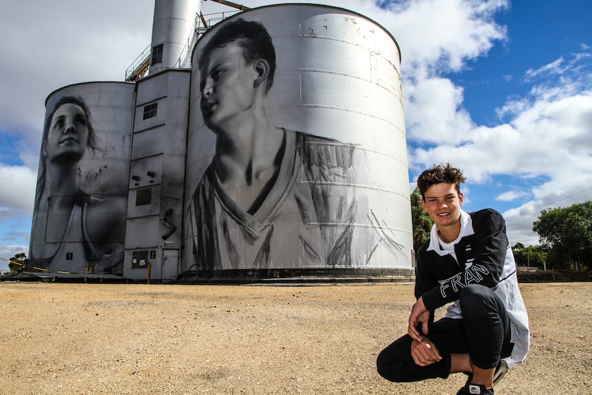 Jordan Weidemann crouching in front the giant steel silo bins.