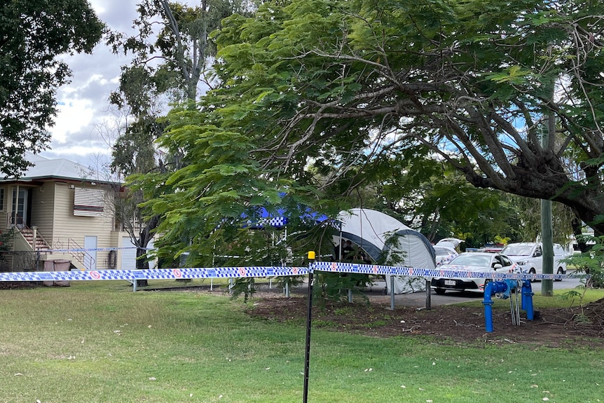 A house with trees covering, with police tape in front of it and a forensics tent in the front yard.