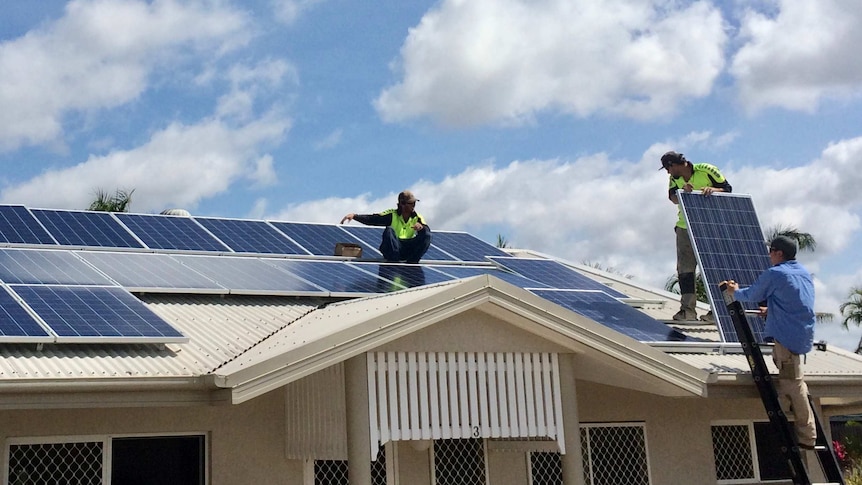 Workers in yellow visibility clothing  install solar panels on the roof of a home.