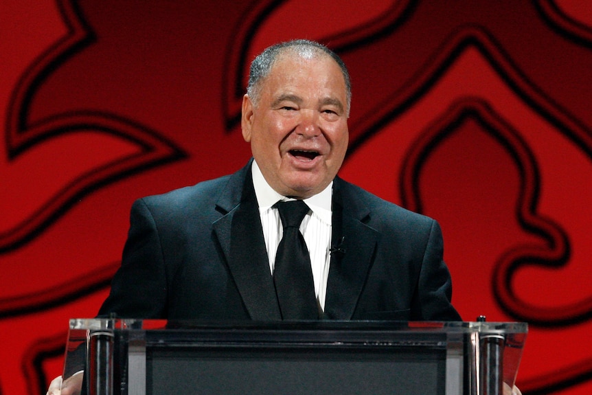 Raul Yzaguirre smiles while speaking behind a black lectern