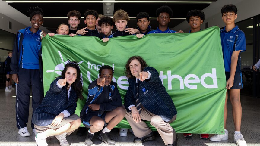 Triple J Unearthed winner LEE. with school mates in front of green Unearthed banner,