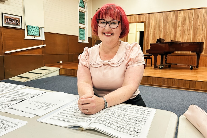 A woman sits at a desk covered in sheet music