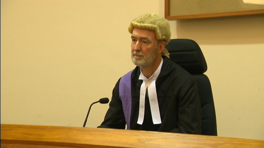 A judge in a wig and robe, sitting in a courtroom