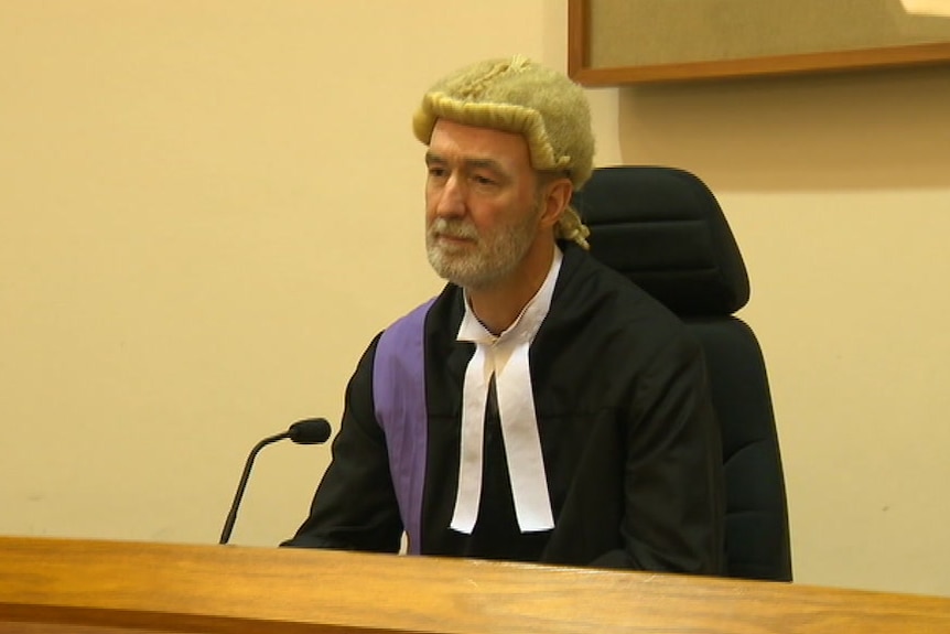 A judge in a wig and robe, sitting in a courtroom