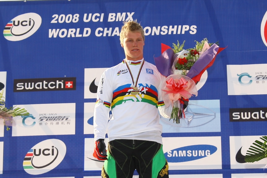 Sam Willoughby holds a bouquet of flowers while wearing a rainbow jersey