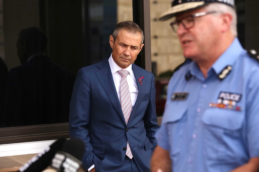 Roger Cook leans against a wall of parliament listening to Chris Dawson speak at a media conference.