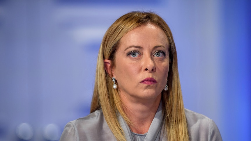 portrait of giorgia meloni staring intently with grey blouse against blue background