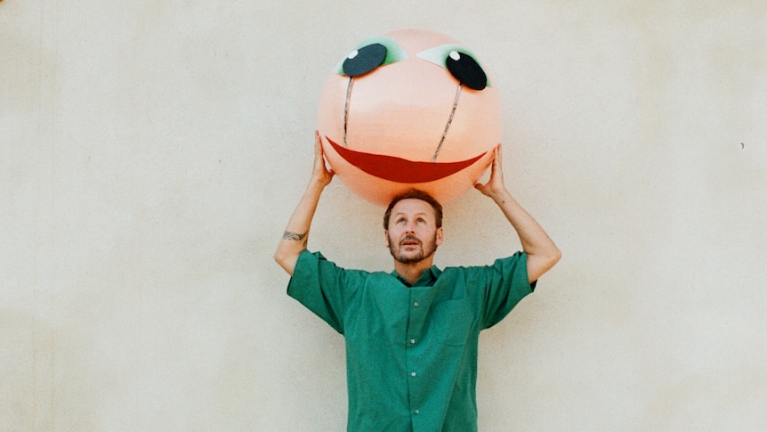 A man in a green shirt holding aloft an inflatable ball with a face on it