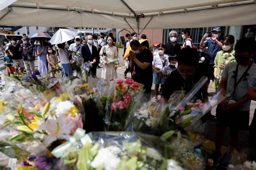 Les gens font la queue pour déposer des fleurs sur une table et prient sur le site où l'ancien Premier ministre est décédé.