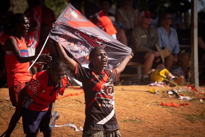 A young woman holding a flag for her team shouting from the sidelines.