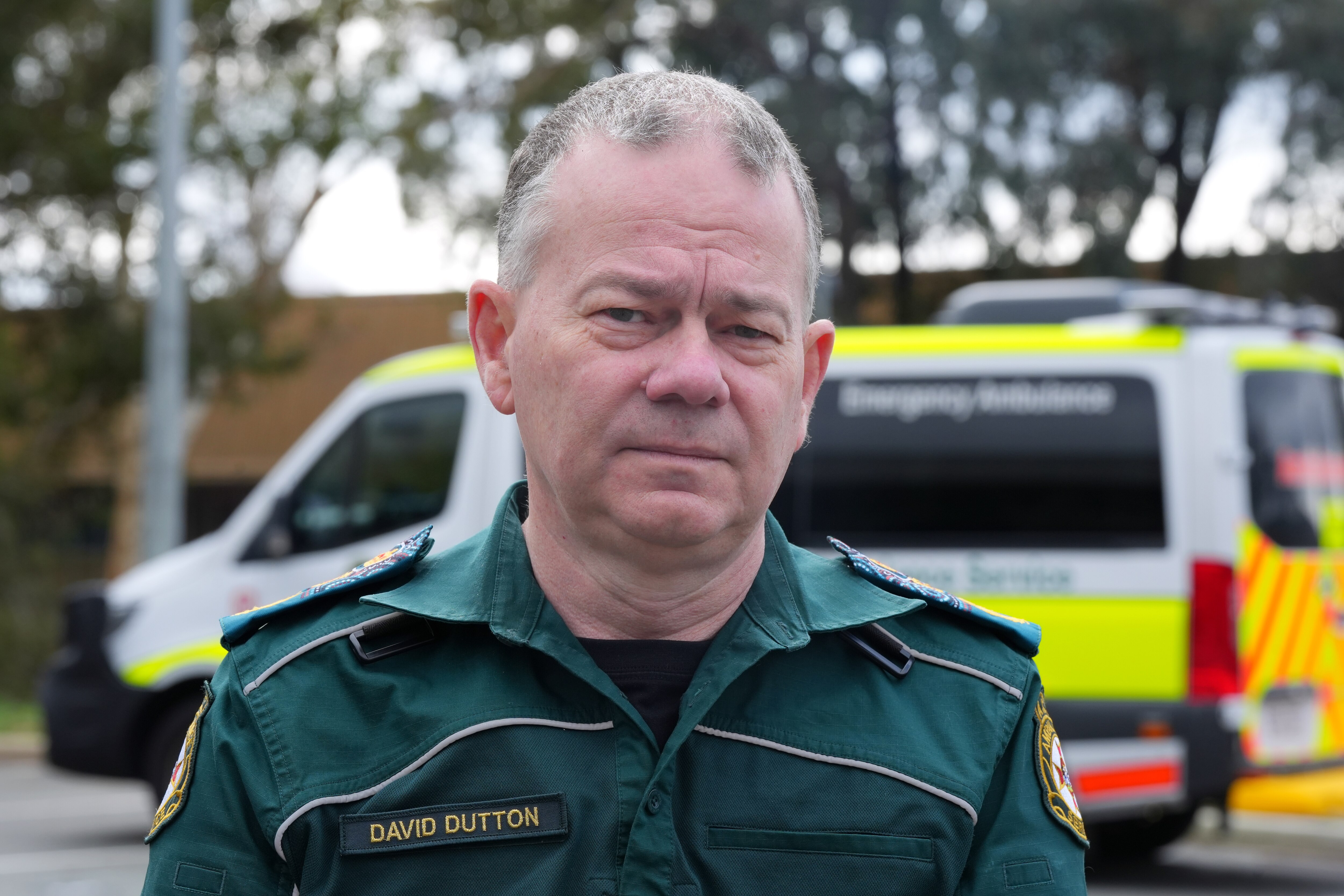 A man wearing an ambulance uniform standing in front of an ambulance van.