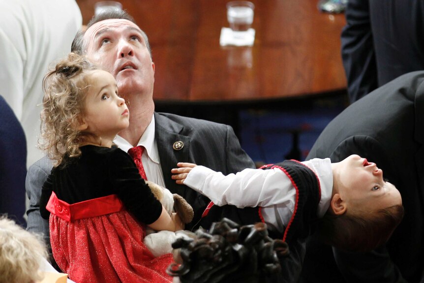 Trent Franks sits in the US House of Representatives with his two young children on his lap.