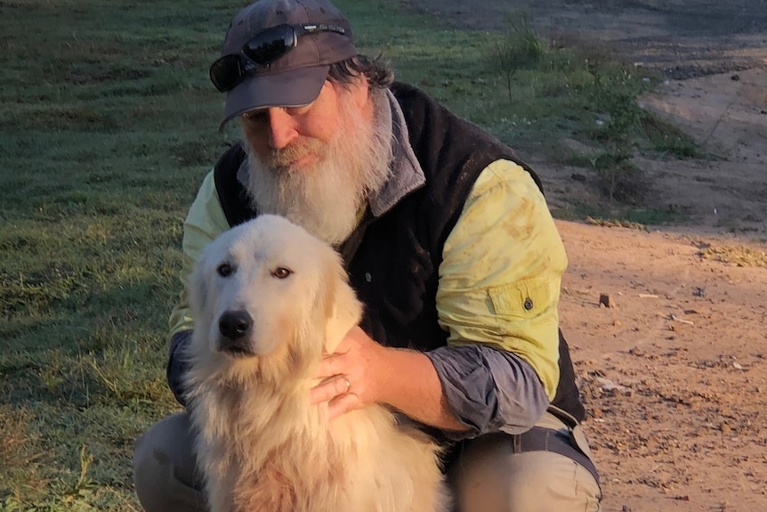 A man with a beard and cap patting a white dog