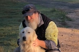 A man with a beard and cap patting a white dog