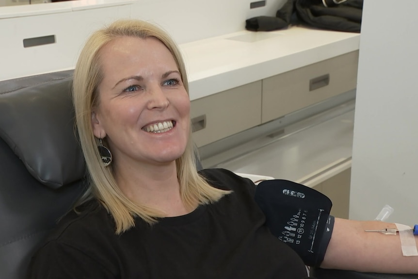 A woman with short blonde hair sitting in a chair having her blood taken.  