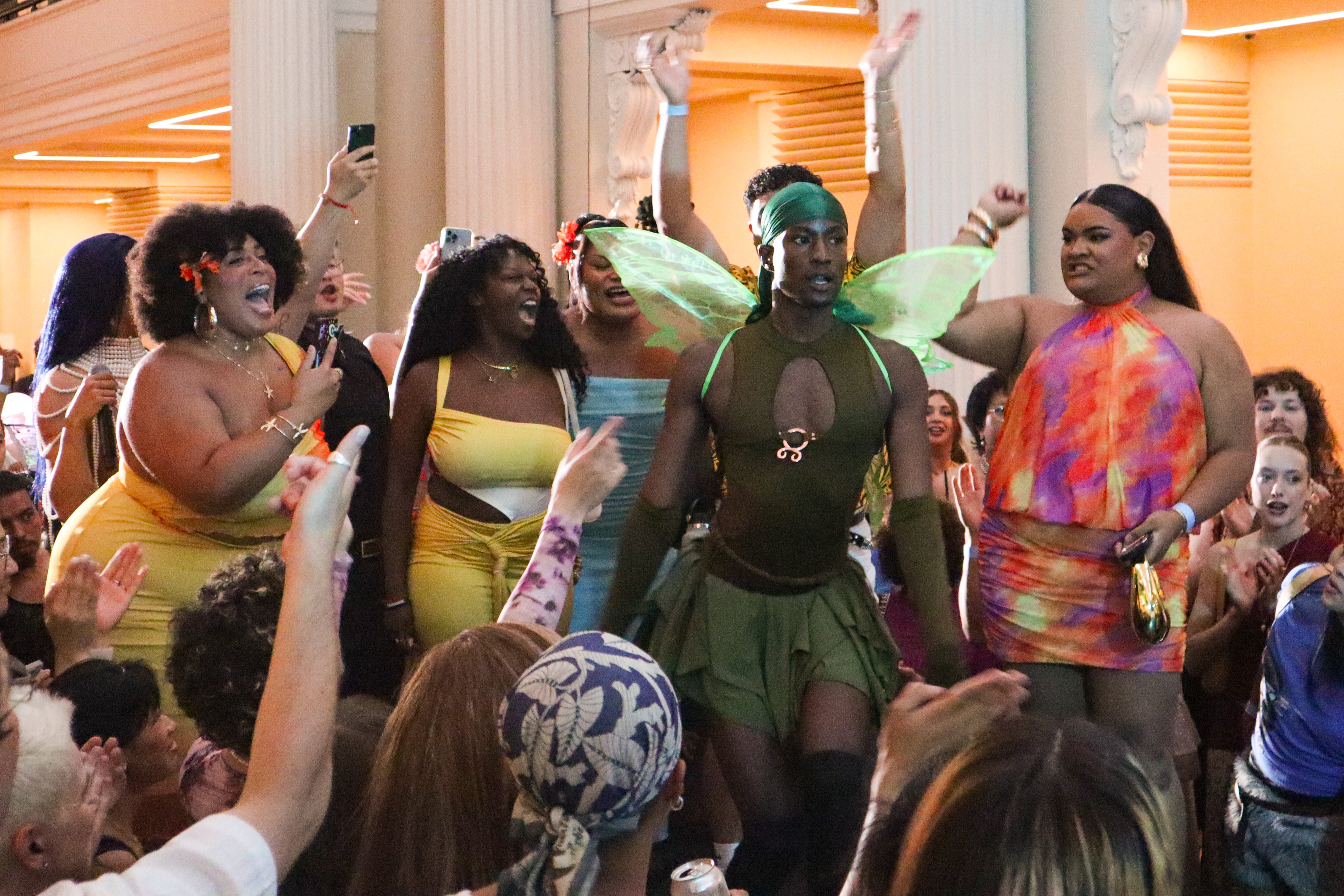 Una persona vestida con un disfraz de hada verde rodeada de otras personas que lo celebran.