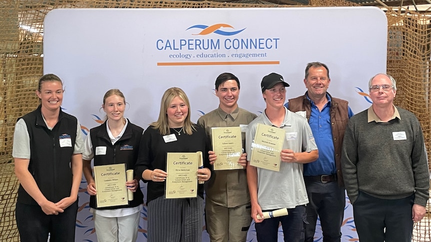 Four students hold their certificates while posing for a picture with Calerpum Station staff