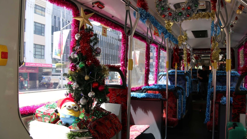 A bus interior featuring masses of pink and blue tinsel, Christmas trees and a stuffed toy Minion.