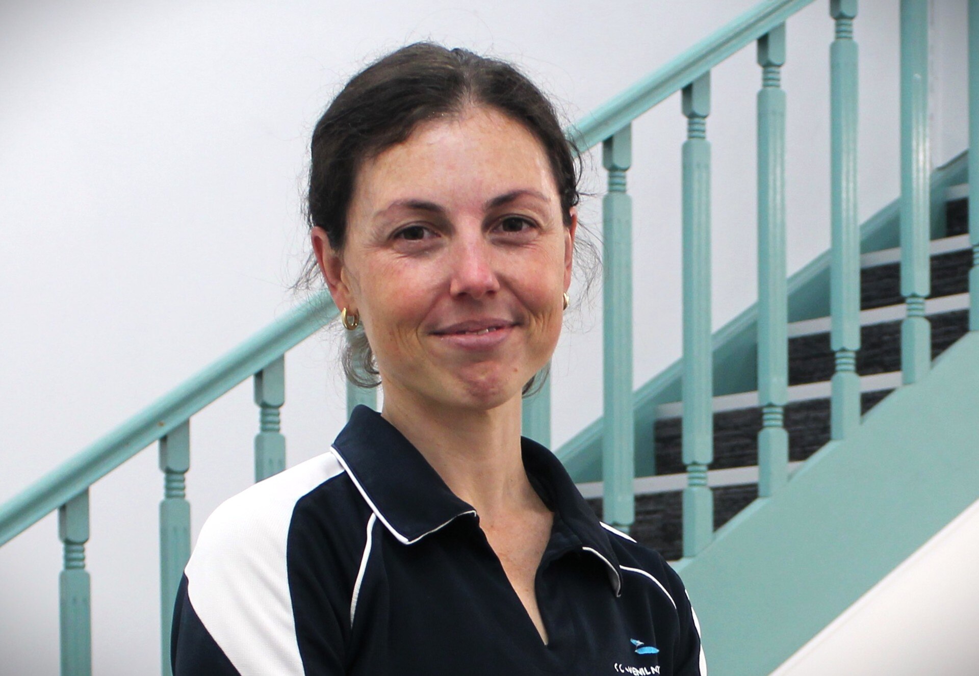 Mulher sorridente, com cabelos escuros, vestindo uma camiseta preta e branca
