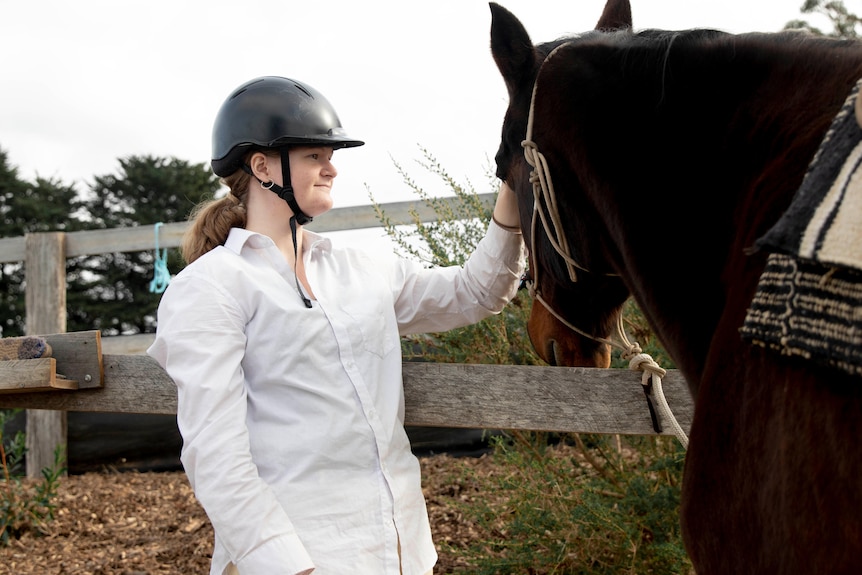 Teenage girl pats horse's face.