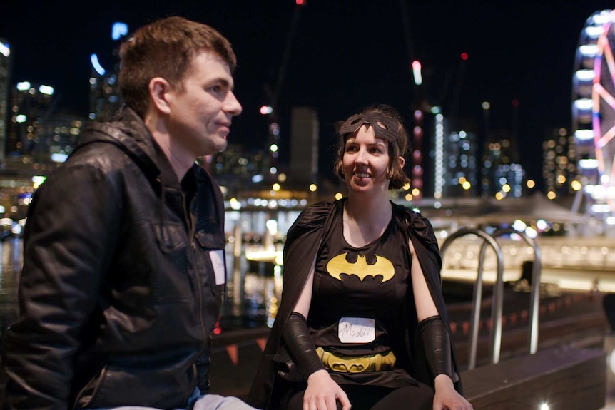 A young woman wearing a batgirl costume is chatting with a young man in a leather jacket