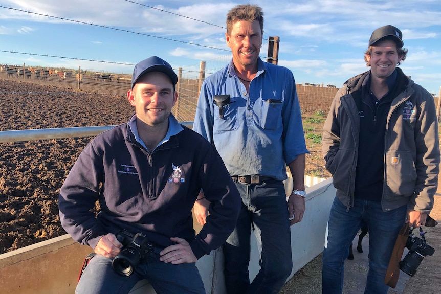 Three men sit and stand near a trough that is used for feeding cattle.