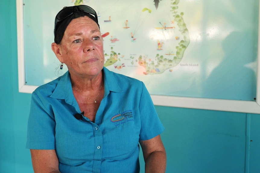 Women in Blue shirt in front of map of the Cocos Islands looks pensively away from the camera. 
