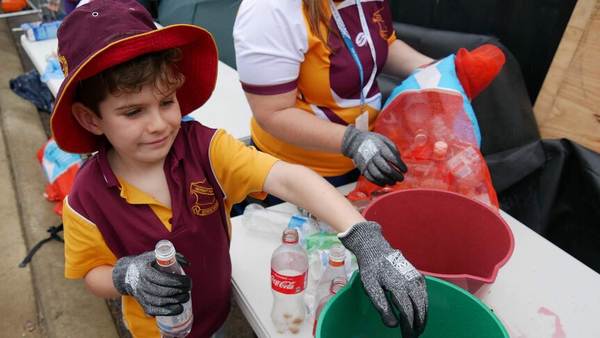 A primary school student wearing gloves removes the lids of plastic bottles and collects them in a bucket.