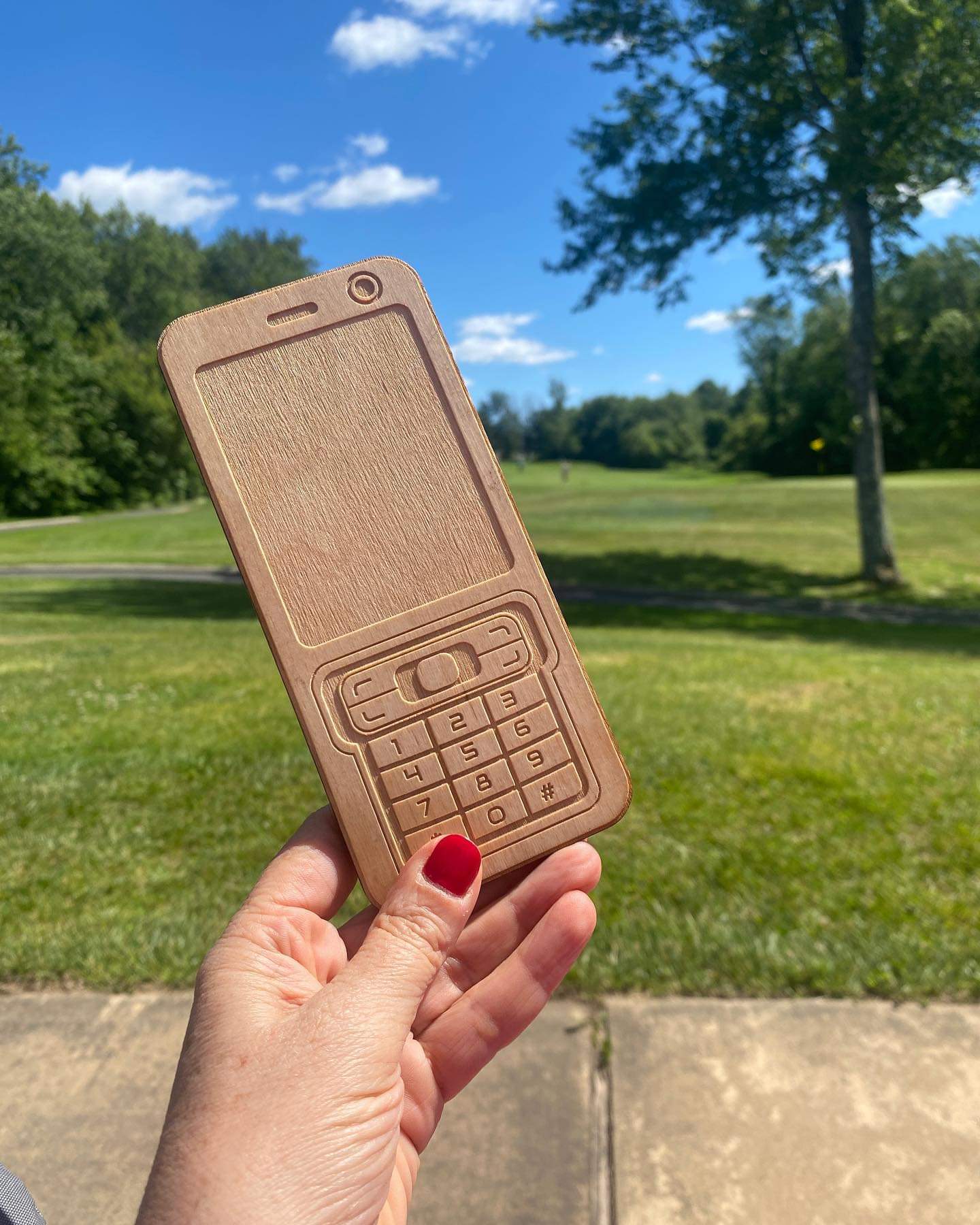 A hand holding a wooden mobile phone in a park.