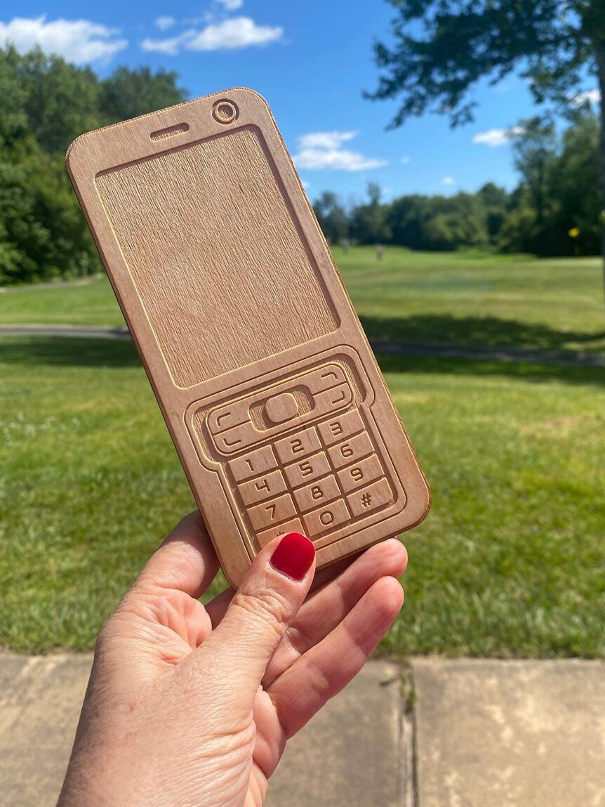 A hand holding a wooden mobile phone in a park.