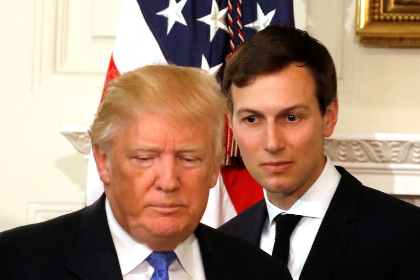 Jared Kushner stares blankly as he walks behind Donald Trump's head in the white house near an american flag