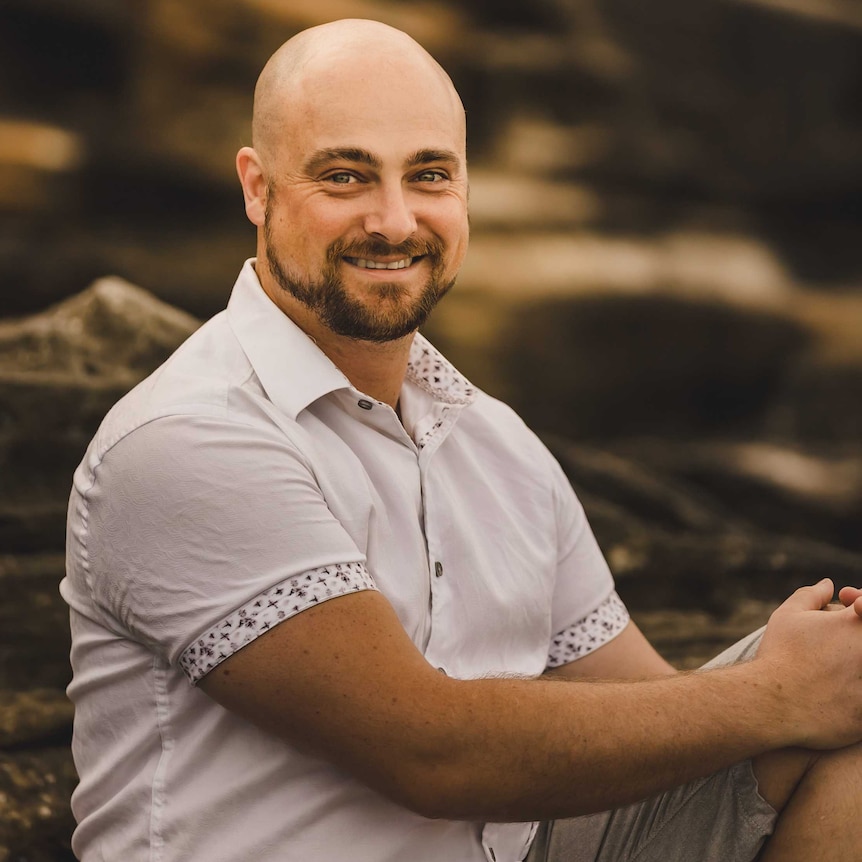 Man sits on rocks with cliff in the background.